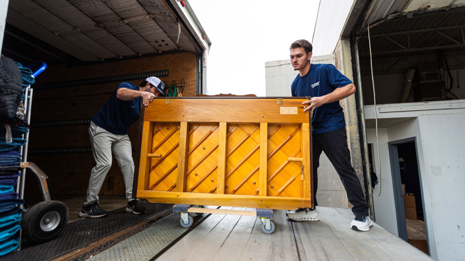 two men putting a piano on a moving truck